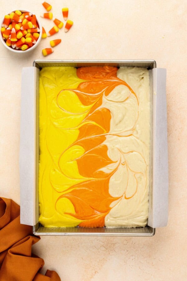 Cake mix is lined up in three different colors in a baking dish - yellow, orange, and white.