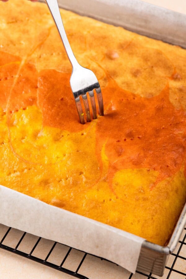 A fork is poking holes in a cake with syrup on top.