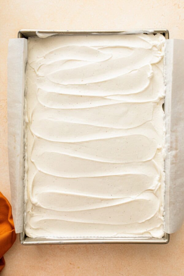 Whipped cream cheese frosting spread evenly across the top of candy corn cake.