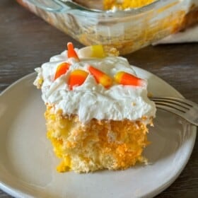 A slice of candy corn cake with whipped cream cheese frosting and candy corn sprinkled on top.