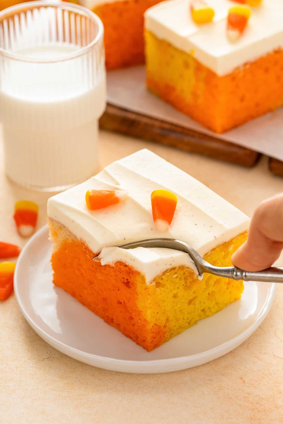 Frosted candy corn poke cake topped with frosting and candy.