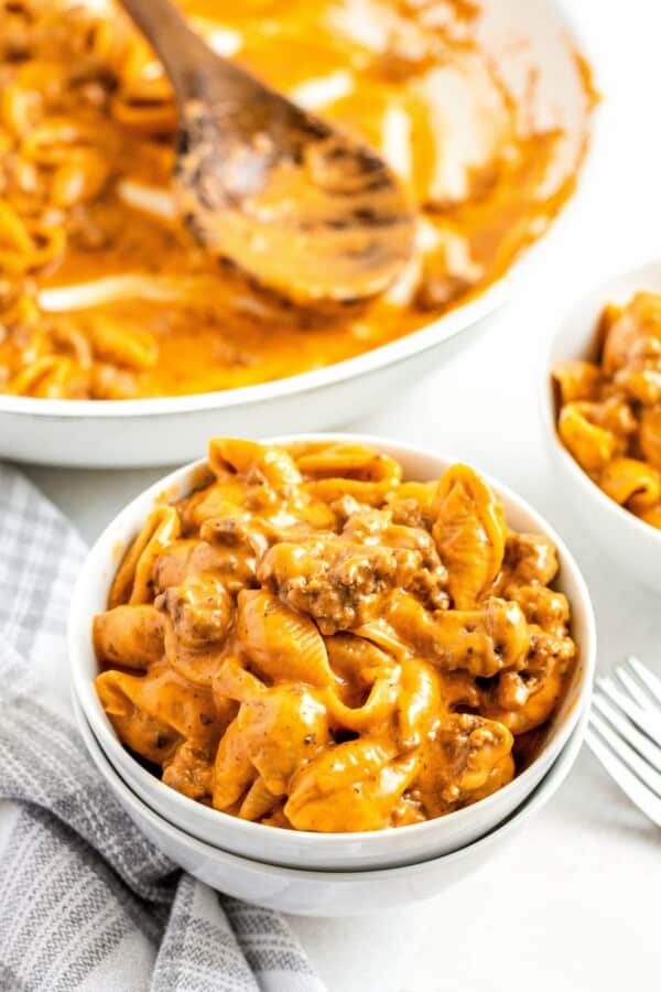 A bowl of creamy cheeseburger hamburger helper with ground beef and an almost empty skillet in the background.