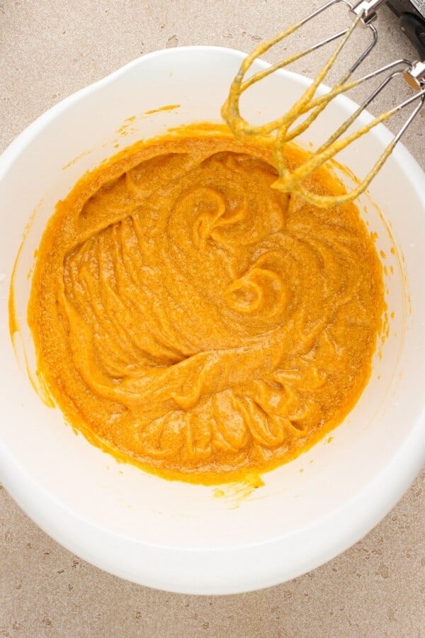 Pumpkin cake batter beat with a hand mixer in a bowl.