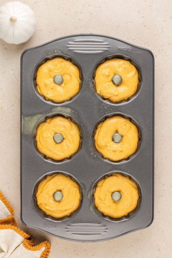 A mini bundt cake pan is filed with portions of pumpkin cake batter.