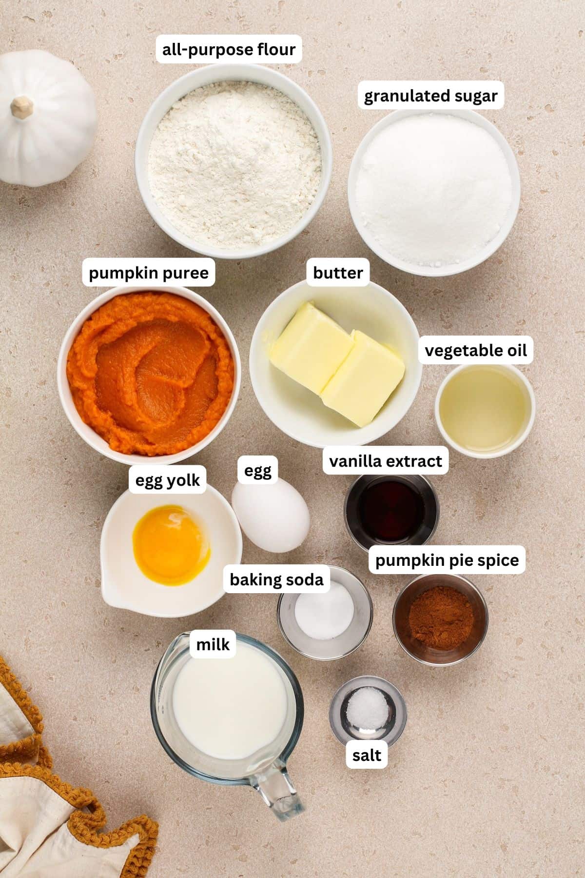 The ingredients for mini pumpkin bundt cake recipe in order from top to bottom: all purpose flour, granulated sugar, pumpkin puree, butter, vegetable oil, egg yolk, egg, vanilla extract, milk, baking soda, pumpkin pie spice and salt.