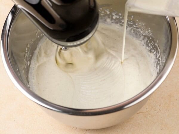 Heavy cream is being poured into frosting mixture in a stand mixer.