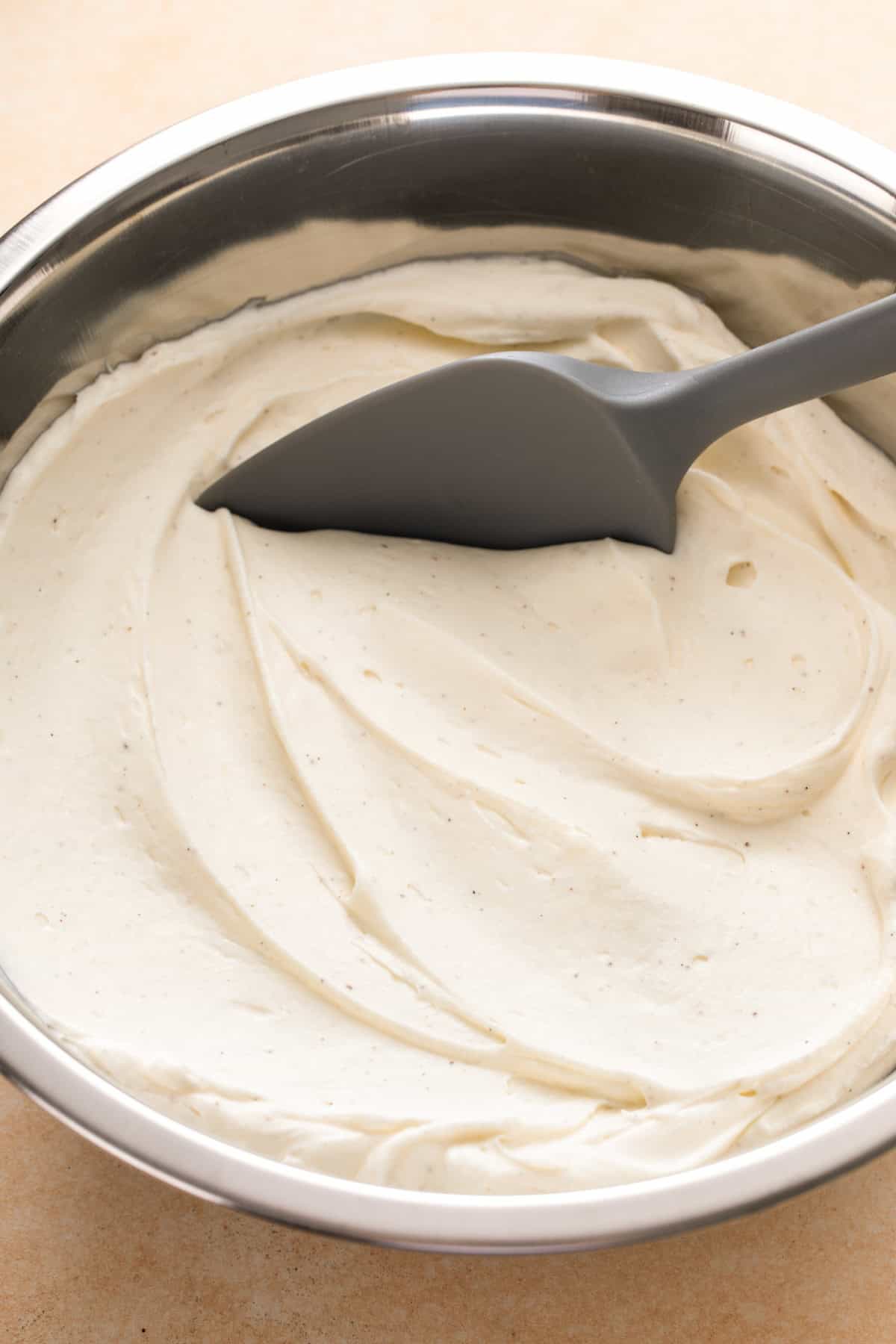 Rubber spatula is mixing whipped cream cheese frosting in a large bowl.