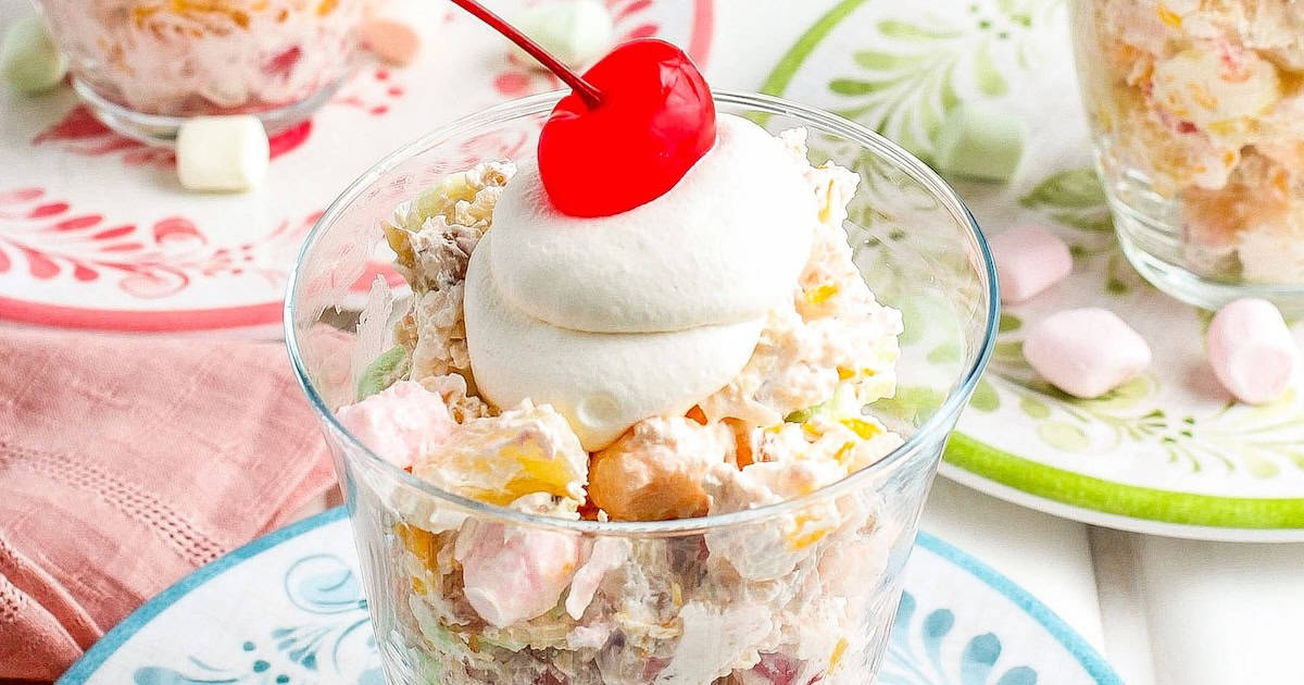 A bowl of ambrosia salad (fruit salad with marshmallows) with whipped cream and a cherry on top.