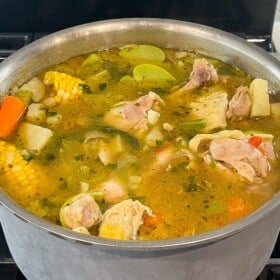 A stockpot of caldo de pollo simmering on a stove top.