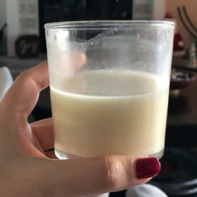 A glass of chilled Coquito (Puerto Rican eggnog) being held by a hand.