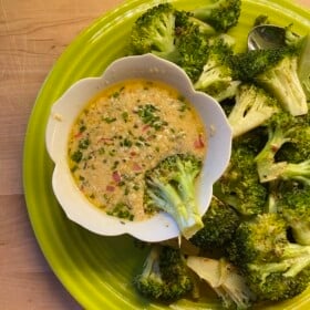 A piece of broccoli being dunked in a bowl of garlic herb steak sauce.