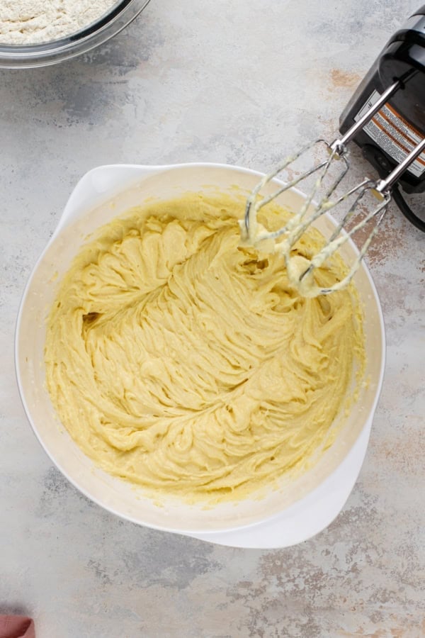 Cake batter in a mixing bowl with a hand mixer on the side with beaters covered in batter.