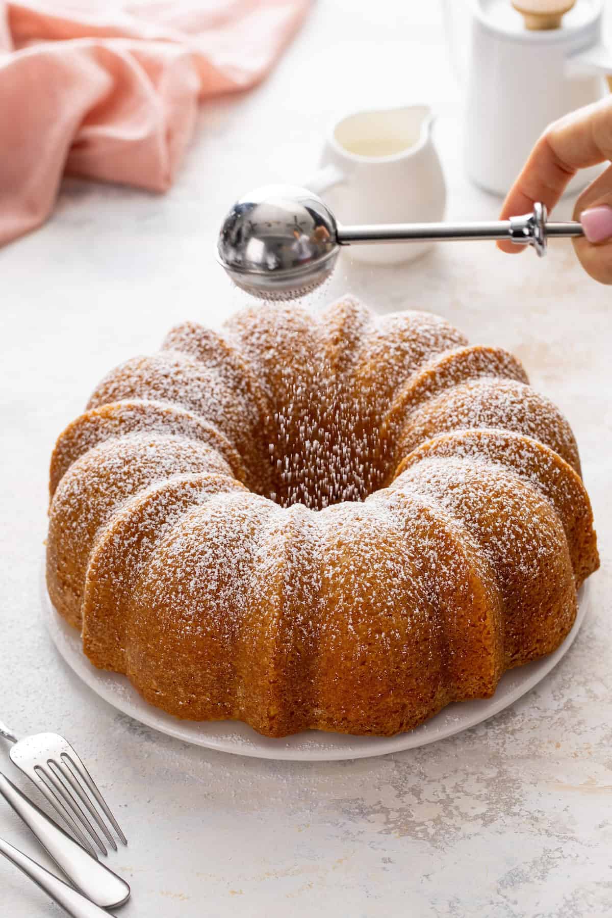 Powdered sugar being dusted over the top of a buttermilk pound cake.