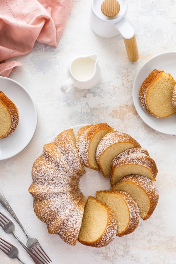 Sliced cake on a platter with powdered sugar dusted on top and two small plates with slices of cake on them for serving.