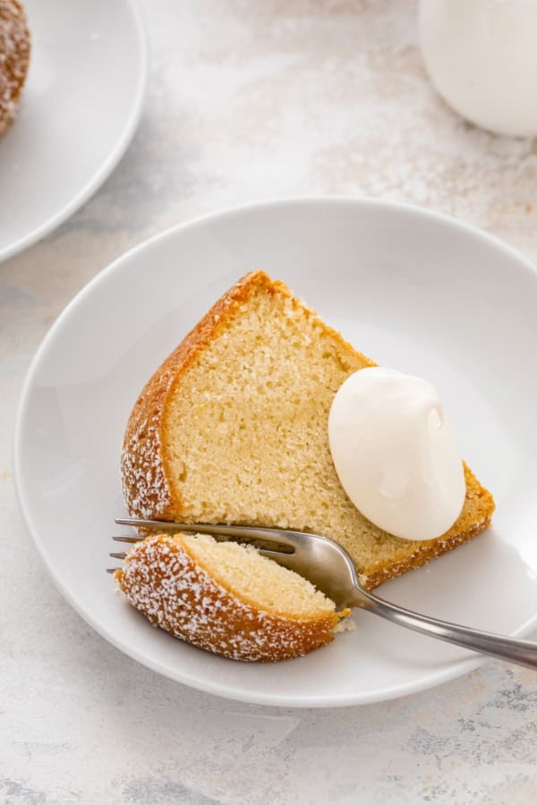 A slice of moist traditional pound cake on a plate with a fork cutting a bite.