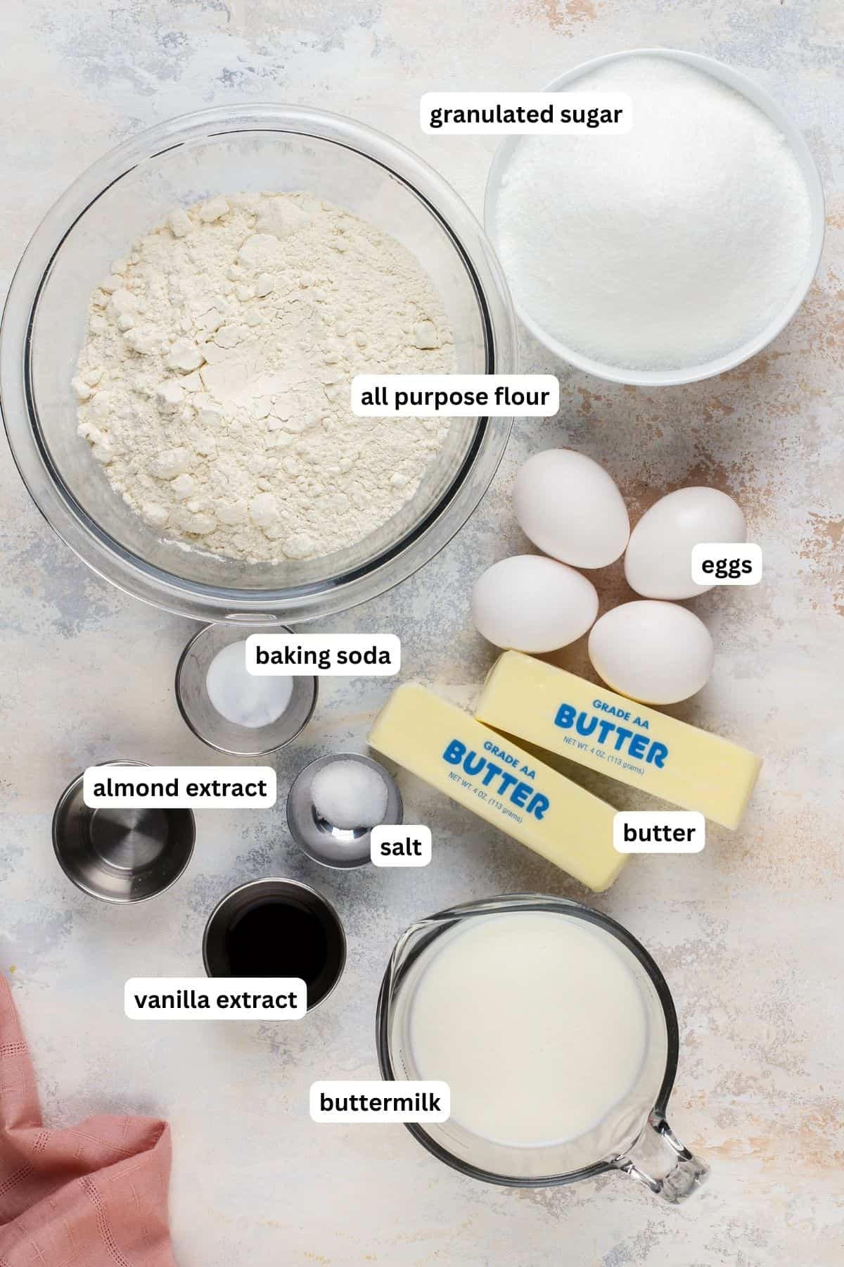 Ingredients arranged in bowls for buttermilk pound cake recipe. From top to bottom: granulated sugar, all purpose flour, eggs, baking soda, almond extract, salt, butter, vanilla extract and buttermilk.