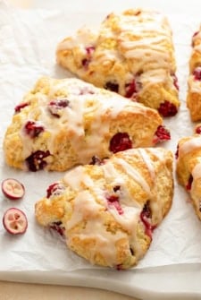 Fresh cranberries are scattered around several orange cranberry scones.