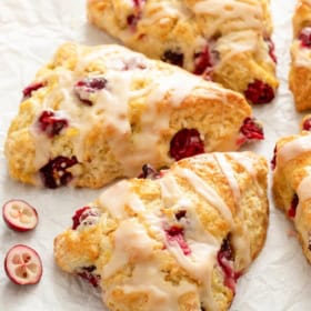 Fresh cranberries are scattered around several orange cranberry scones.