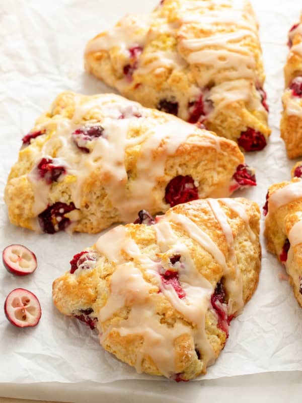 Fresh cranberries are scattered around several orange cranberry scones.