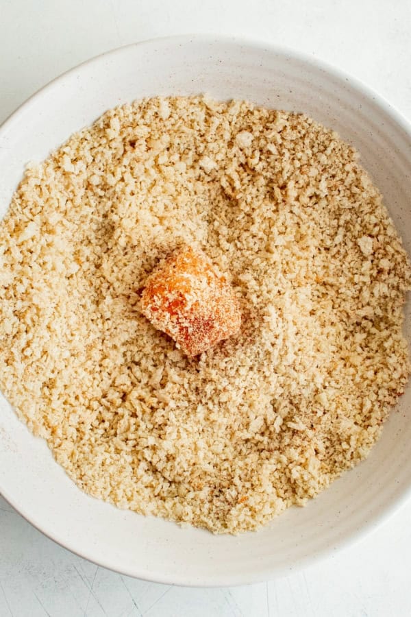 A piece of raw salmon is being coated in seasoned breadcrumbs.