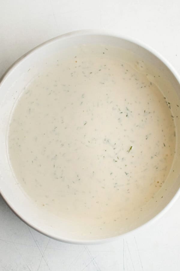 Creamy garlic dill dipping sauce is presented in a small white bowl.