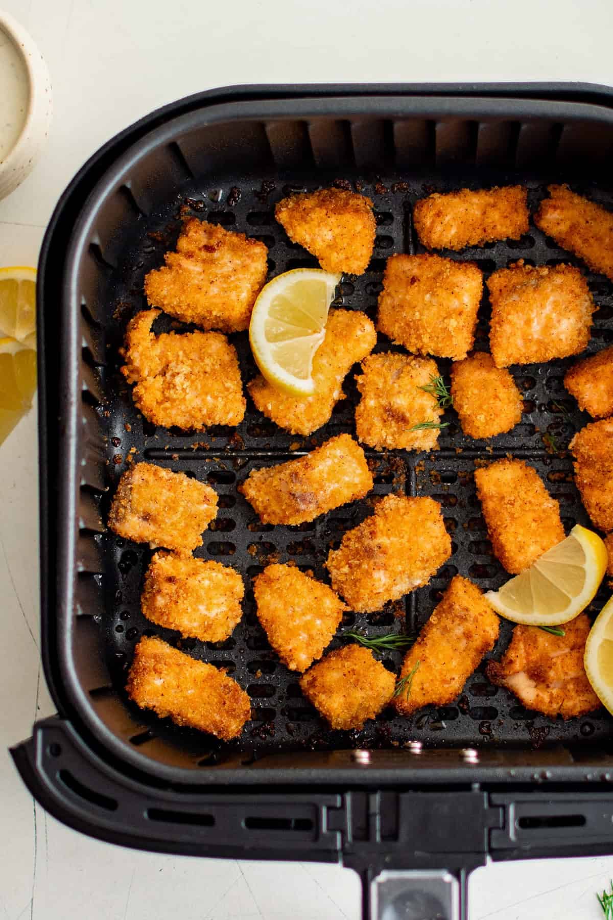 Lemon wedges are placed in the basket of an air fryer with cooked salmon nuggets.