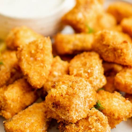 Crispy air fryer salmon bites are served with a small bowl of creamy dipping sauce.