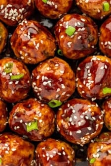 Chopped green onions and sesame seeds garnish a large portion of asian meatballs.