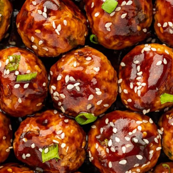 Chopped green onions and sesame seeds garnish a large portion of asian meatballs.