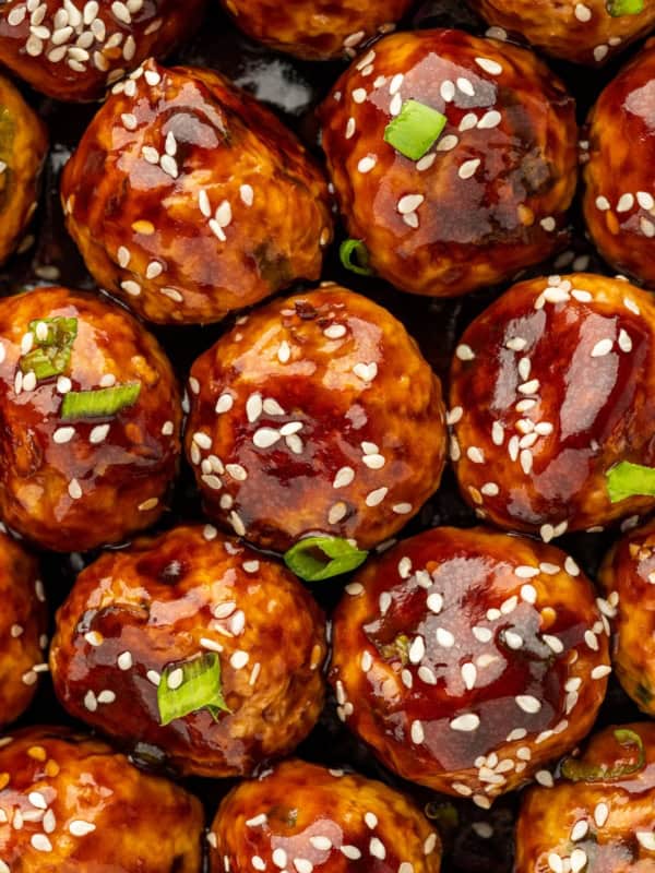 Chopped green onions and sesame seeds garnish a large portion of asian meatballs.