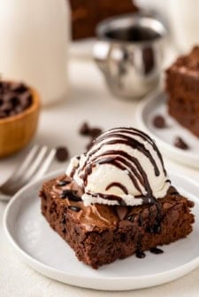 A scoop of vanilla ice cream on top of a homemade brownie is topped with a drizzle of chocolate sauce.