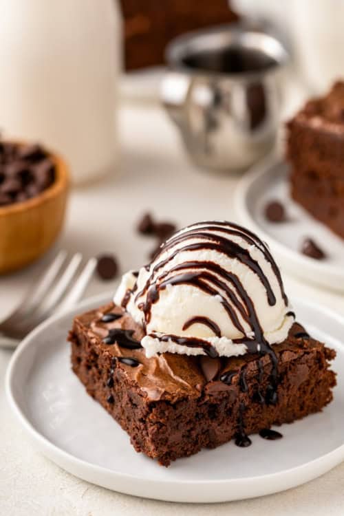 A scoop of vanilla ice cream on top of a homemade brownie is topped with a drizzle of chocolate sauce.