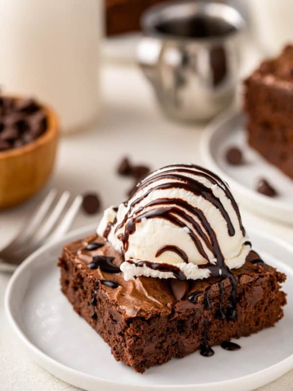 A scoop of vanilla ice cream on top of a homemade brownie is topped with a drizzle of chocolate sauce.