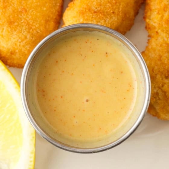 A small bowl of homemade honey mustard sauce with chicken on the side.