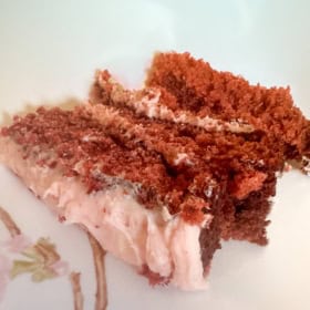 A slice of fresh strawberry cake with strawberry frosting on a plate.