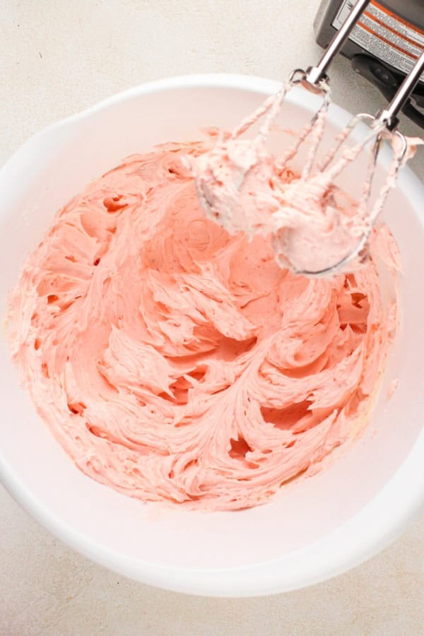 Soft pink strawberry frosting is whipped up in a large white bowl.