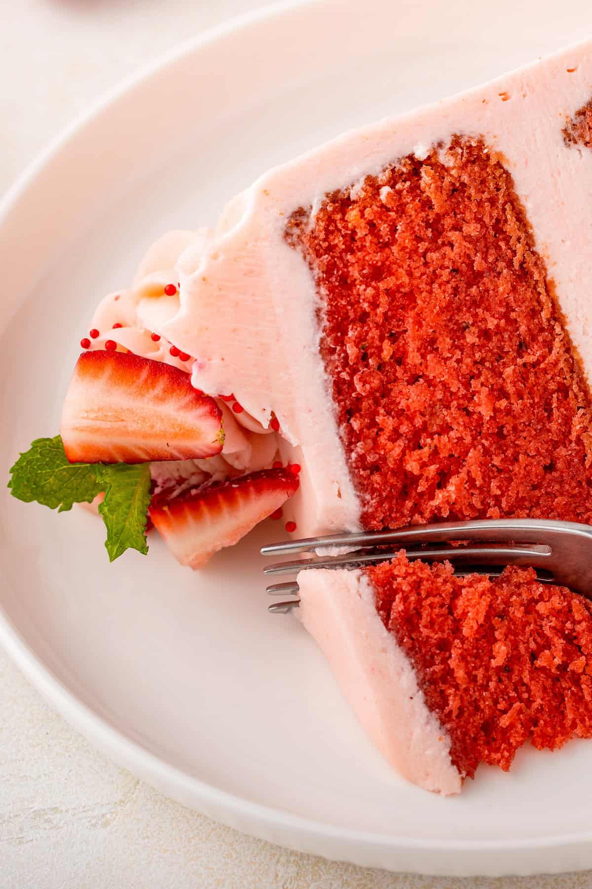 A fork is digging into a slice of vibrant strawberry frosted cake.