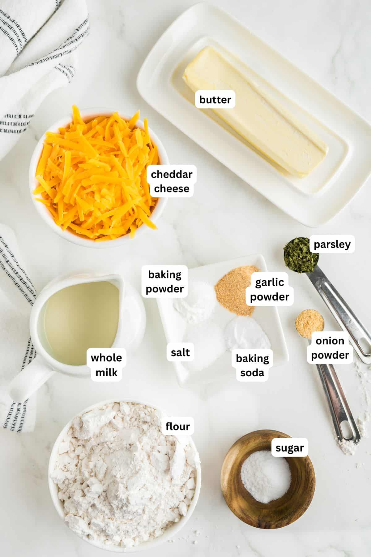 The ingredients for cheddar bay biscuit recipe in order from top to bottom: butter, cheddar cheese, whole milk, baking powder, baking soda, garlic powder, onion powder, salt, parsley, flour, sugar.