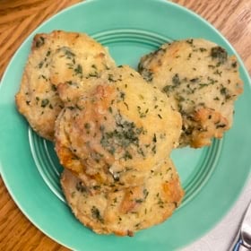 Four cheddar bay biscuits stacked on a plate topped with garlic butter with herbs.