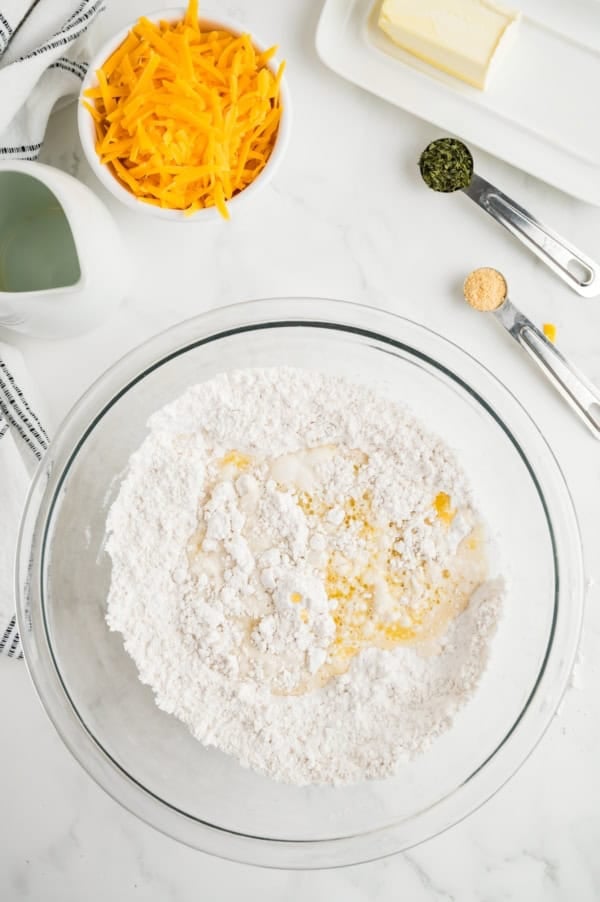 The ingredients for cheddar biscuits are in a glass mixing bowl.