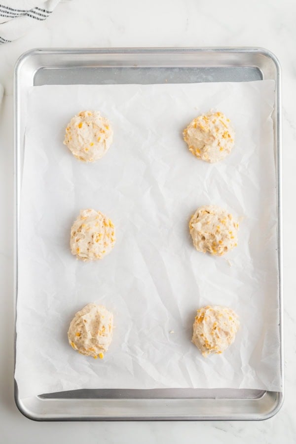 Eight uncooked biscuits are spread on a prepared baking sheet.