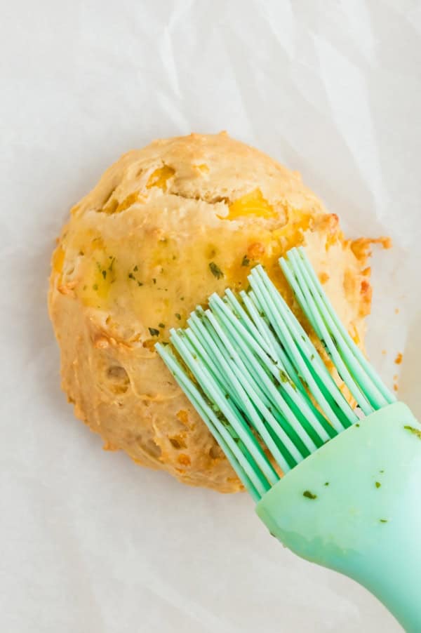 A rubber brush is spreading butter topping on a biscuit.