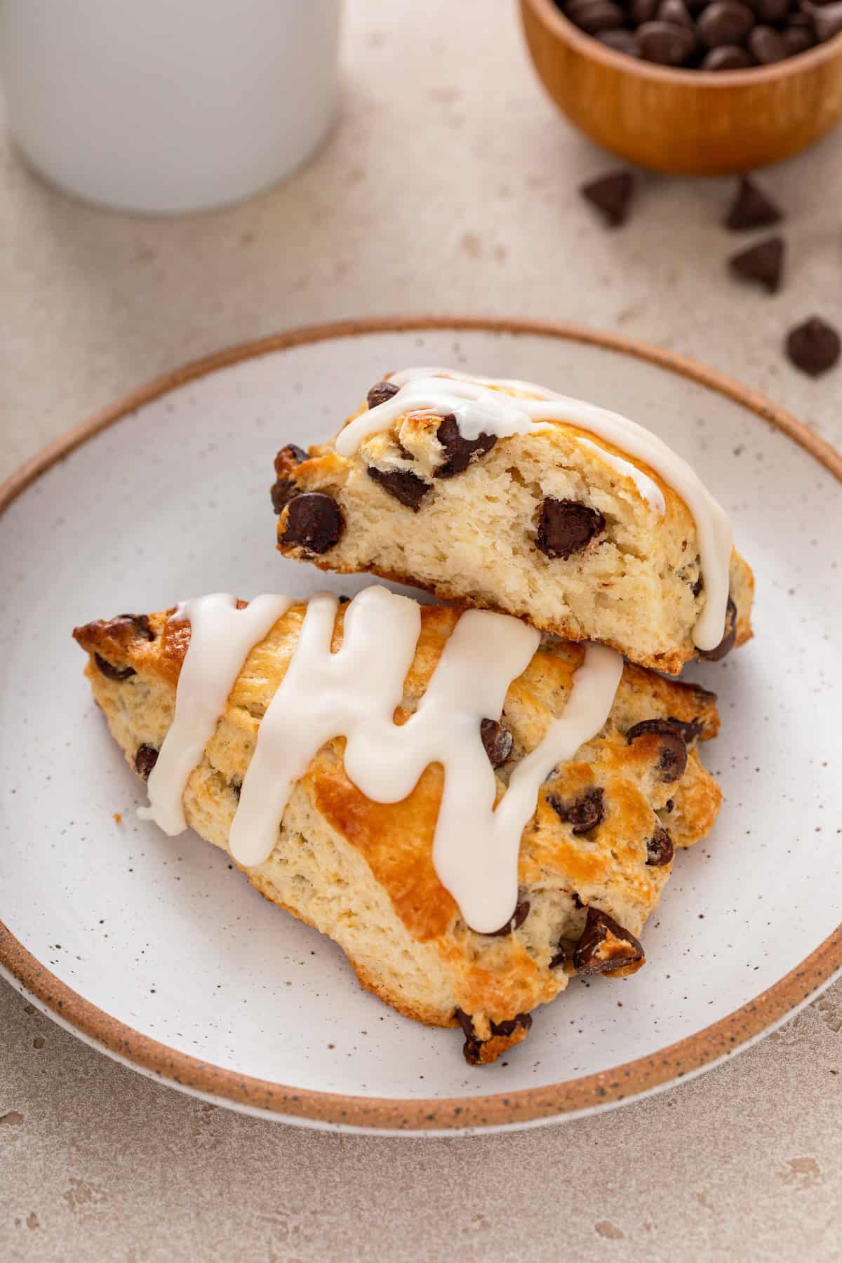 Two scones on a plate with one scone broken in half to show the flaky layers and chocolate chips inside.