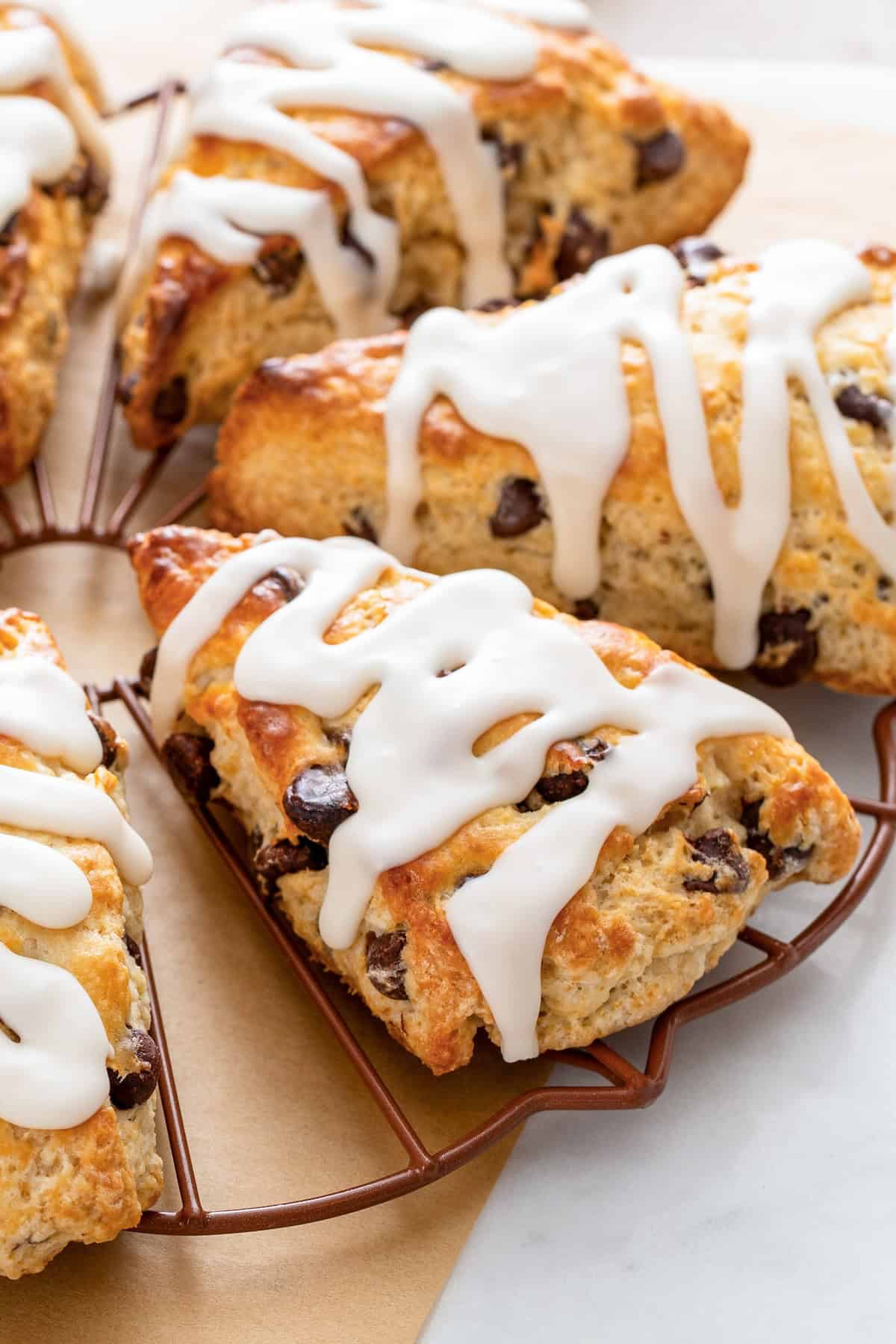 Flaky and golden chocolate chip scones are topped with sweet icing on a wire cooling rack.
