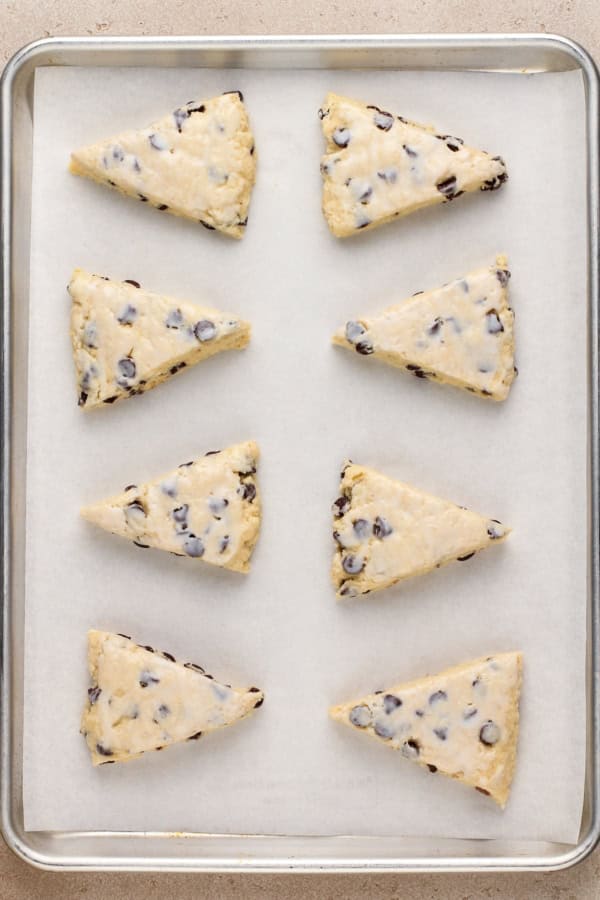 Uncooked chocolate chip scones are spread on a prepared baking sheet.
