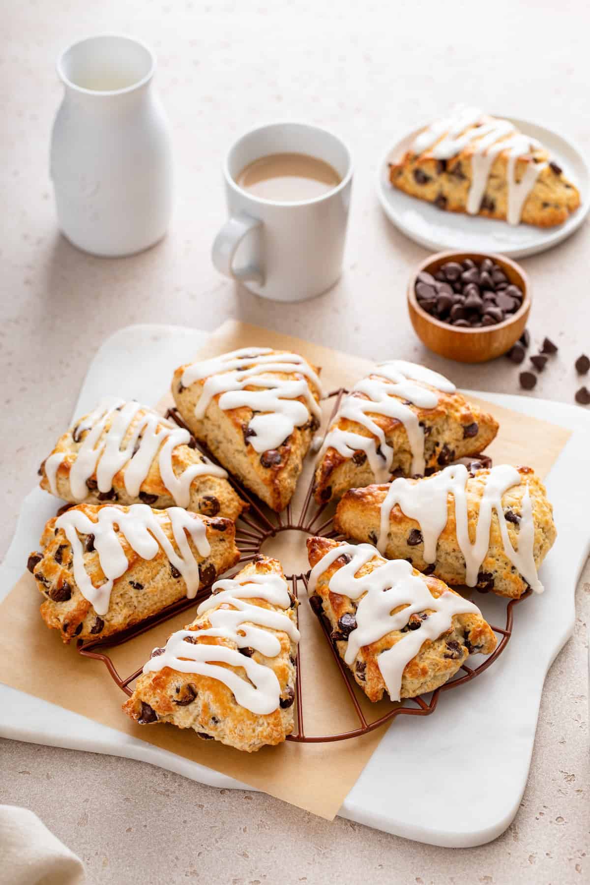 Homemade chocolate chip scones are topped with icing and placed in a neat circle.