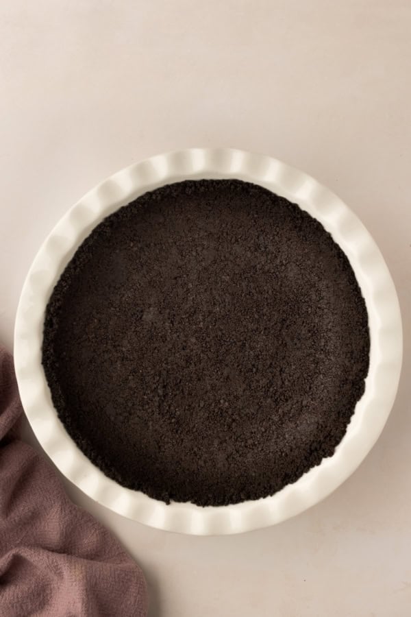 A white pie dish is filled with an Oreo crust.