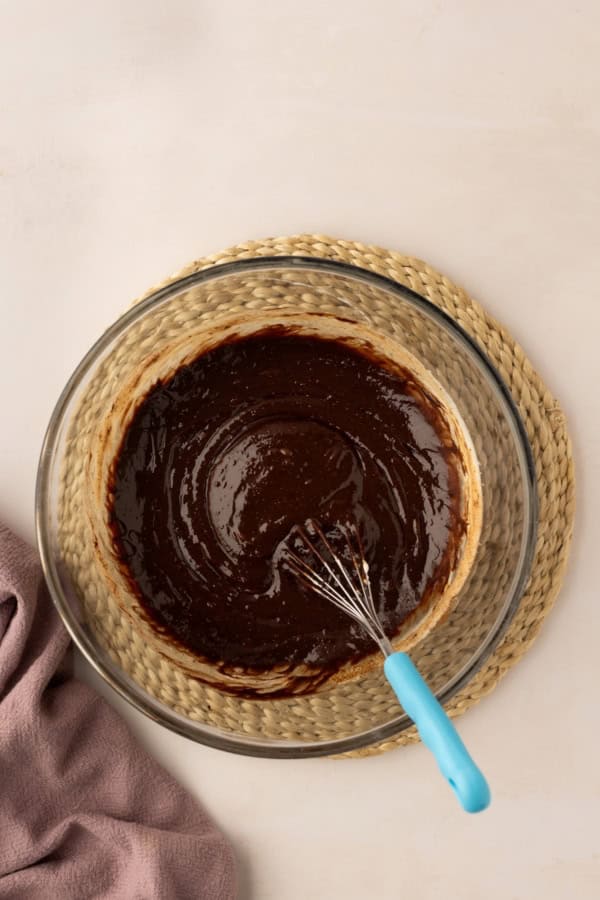 Melted chocolate is whisked in a glass bowl.