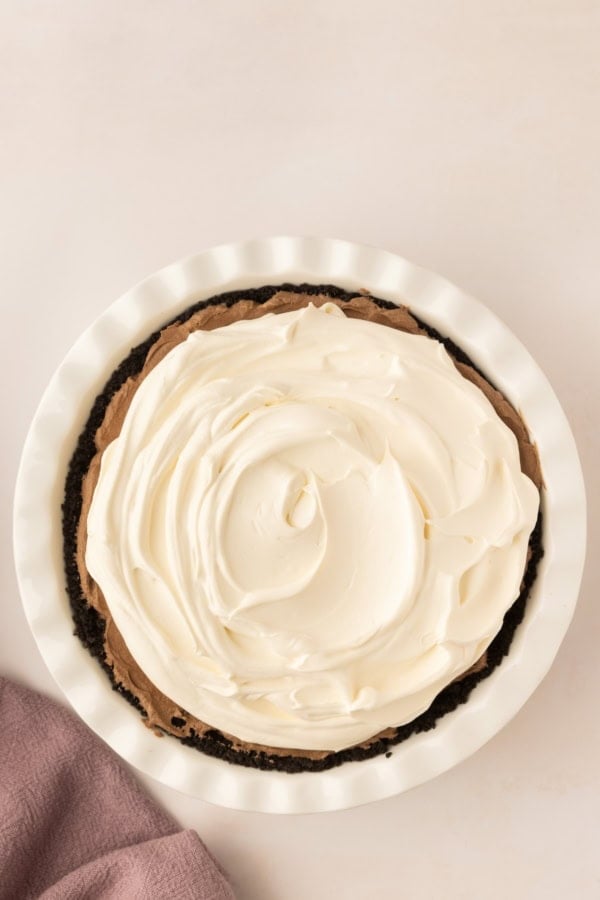 Whipped cream is spread across the top of a silky chocolate pie.