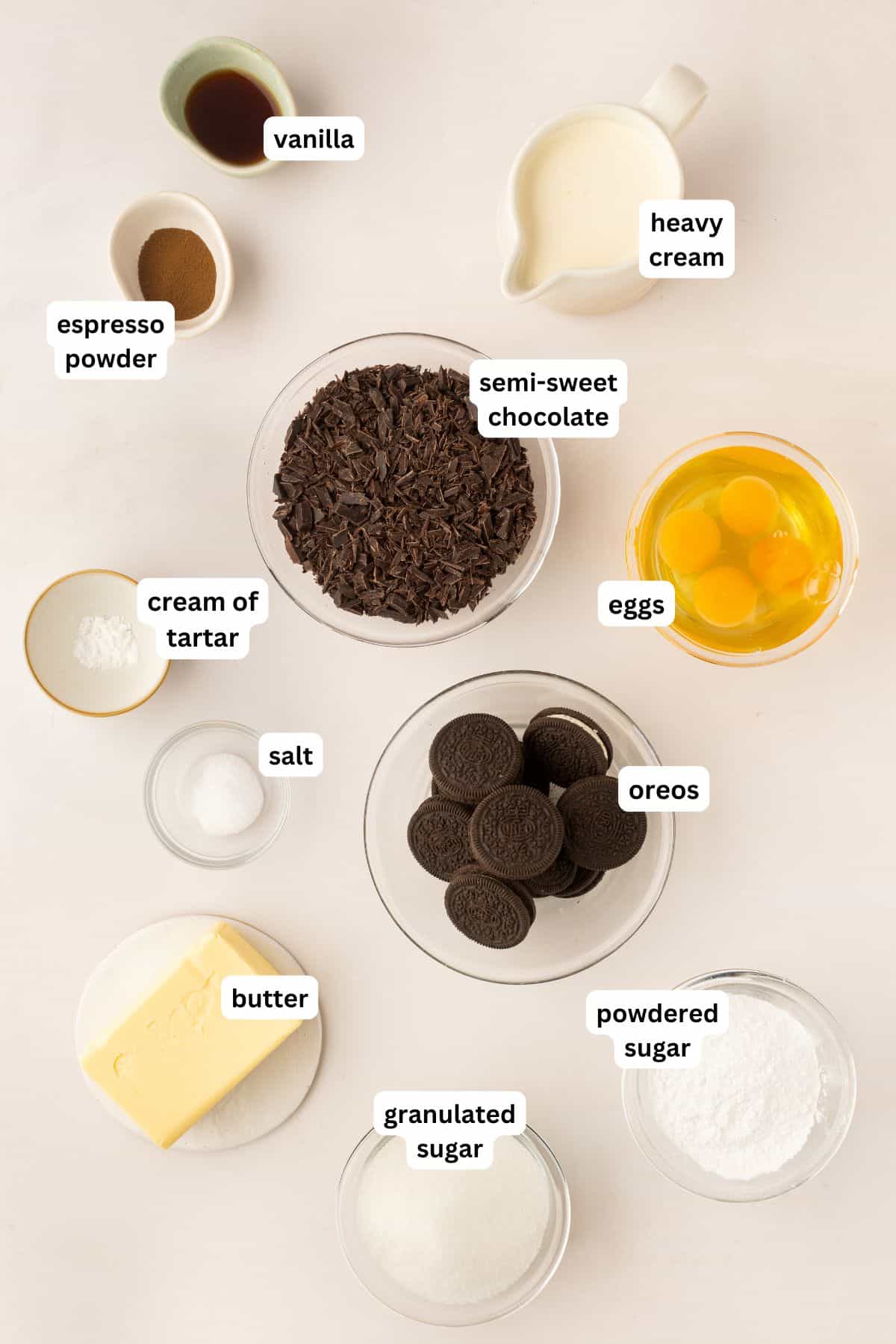 The ingredients for French silk pie recipe in order from top to bottom: vanilla, espresso powder, heavy cream, semi-sweet chocolate, eggs, cream of tartar, salt, Oreos, butter, granulated sugar, powdered sugar.